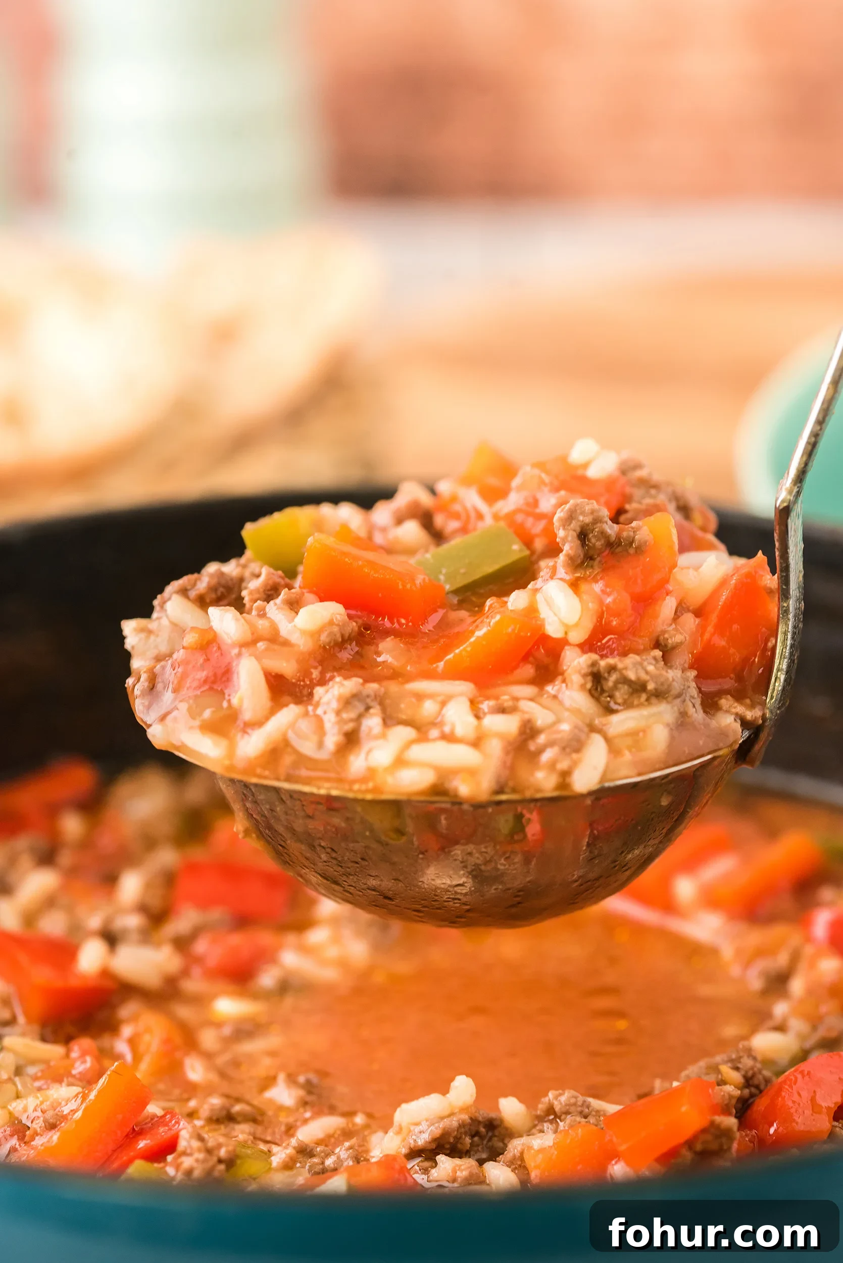 Stuffed Pepper Soup Recipe That Warms the Soul 7 closeup shot of a ladle full of soup, with a wooden background