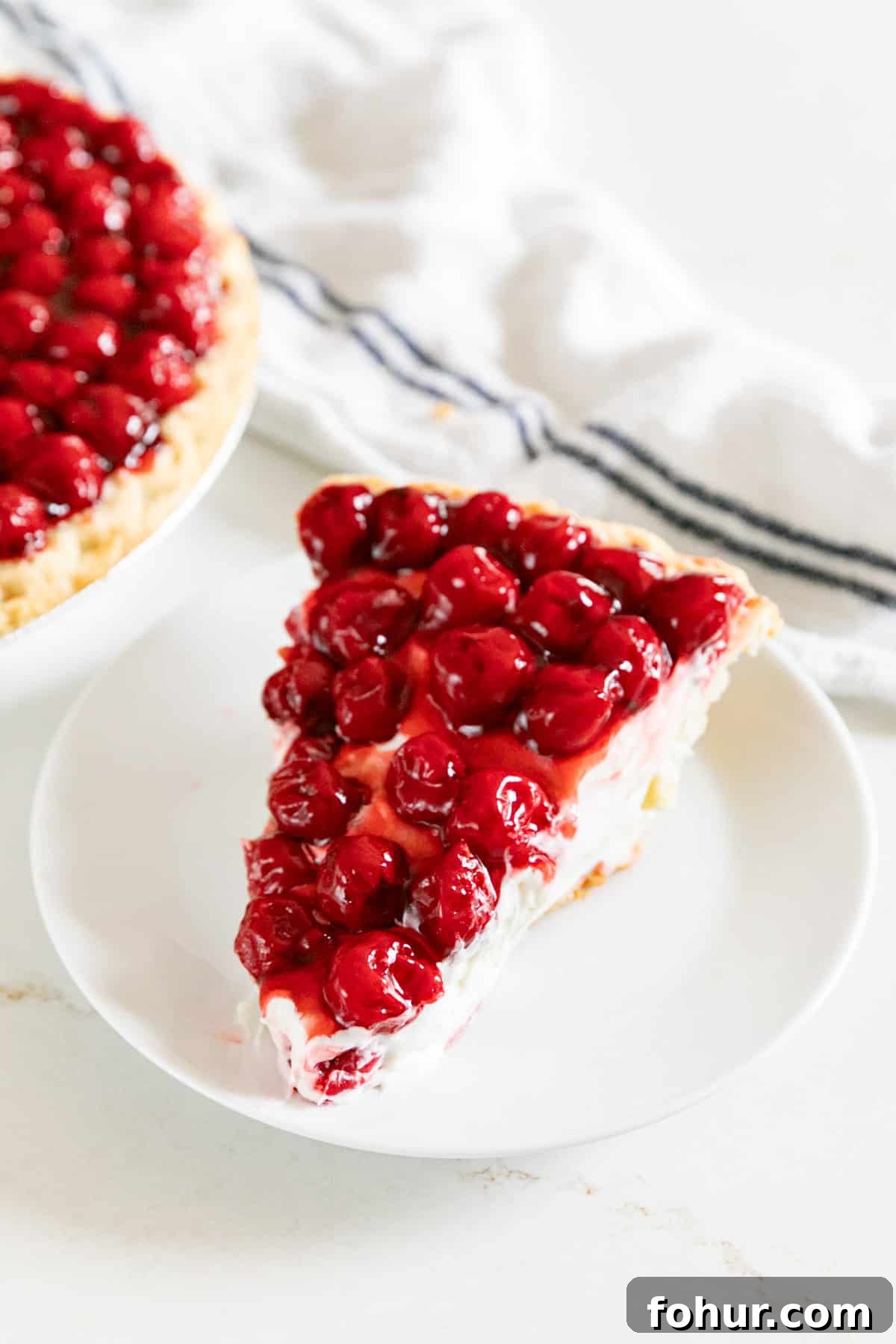 Cherry Cream Cheese Pie Recipe 10 A slice of cherry cheese pie on a white plate with the pie behind it.