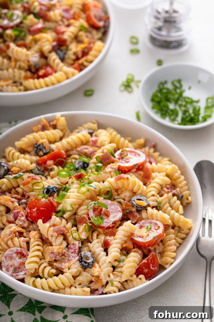 Creamy Bacon Ranch Pasta Salad with Peas and Cheddar 2 White bowl filled with bacon ranch pasta salad on a white countertop, with a second bowl visible in the background.