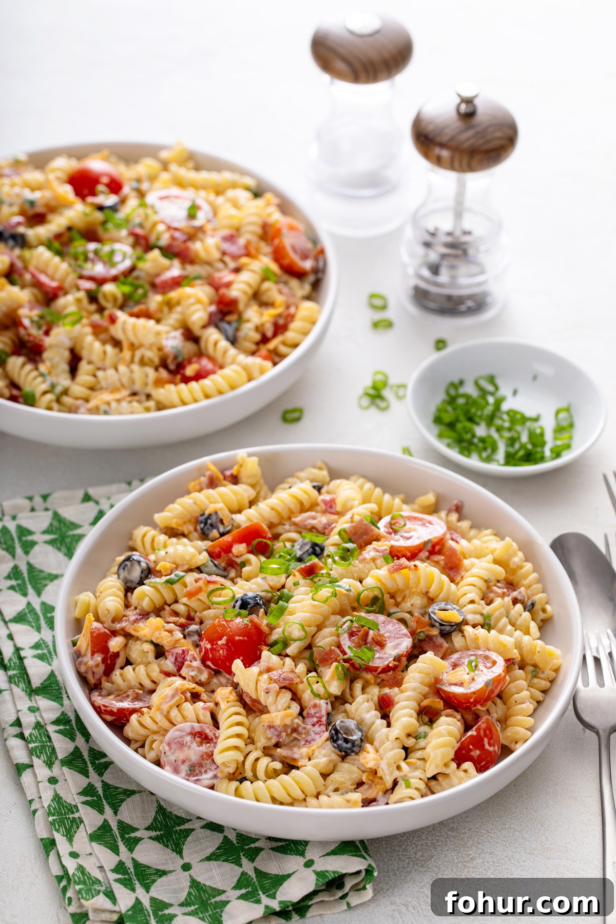Creamy Bacon Ranch Pasta Salad with Peas and Cheddar 10 Two white bowls filled with bacon ranch pasta salad, set on a white countertop with a green and white napkin.