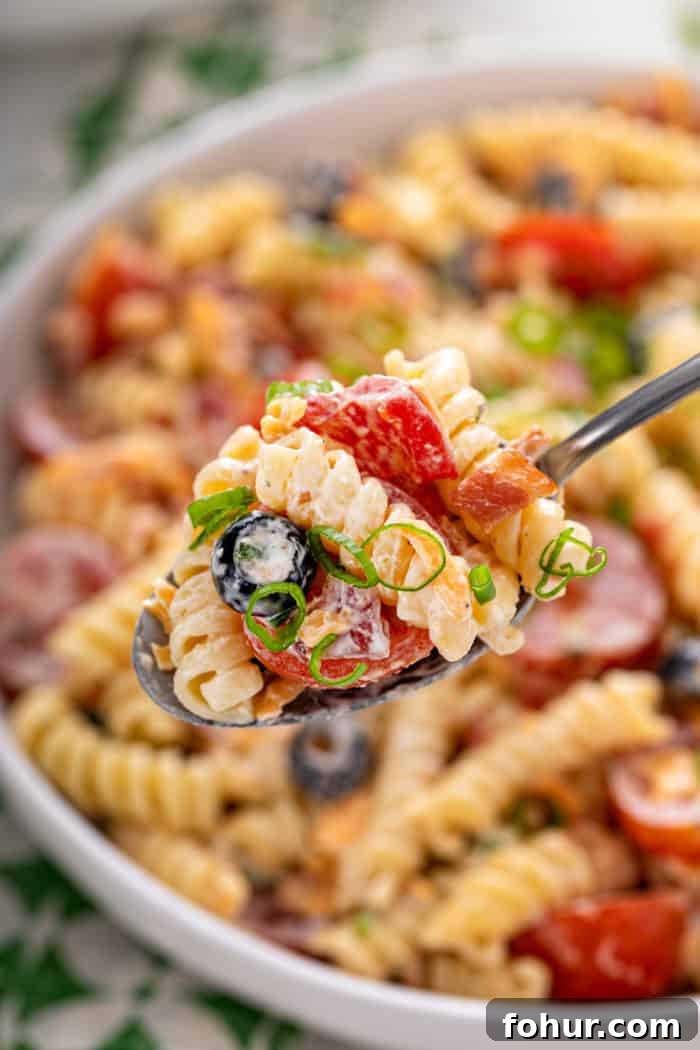Creamy Bacon Ranch Pasta Salad with Peas and Cheddar 3 Spoon holding up a big bite of bacon ranch pasta salad, with a bowl of the salad in the background.
