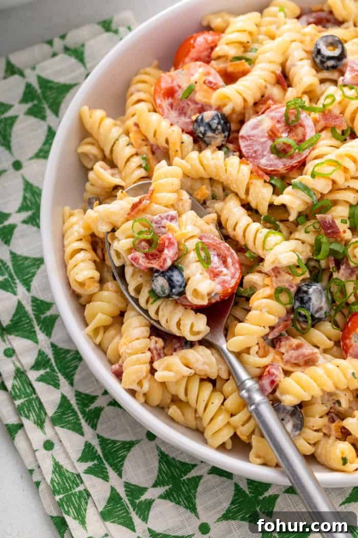 Creamy Bacon Ranch Pasta Salad with Peas and Cheddar 9 Close up of bacon ranch pasta salad in a white bowl. A silver serving spoon is also in the bowl.