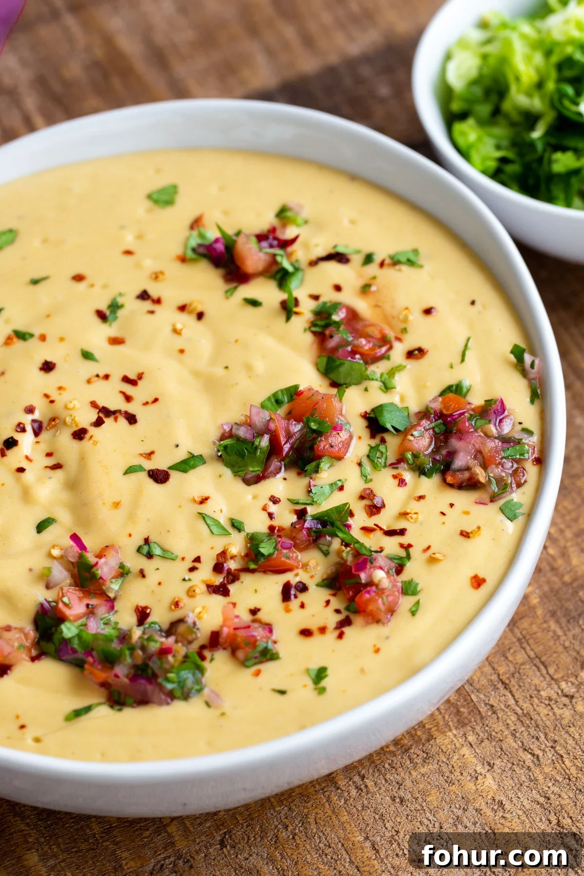 Instant Pot Vegan Cheese Sauce with Potatoes and Carrots 7 a white bowl filled with Instant Pot Vegan Cheese Sauce decorated with fresh chopped herbs and tomatoes