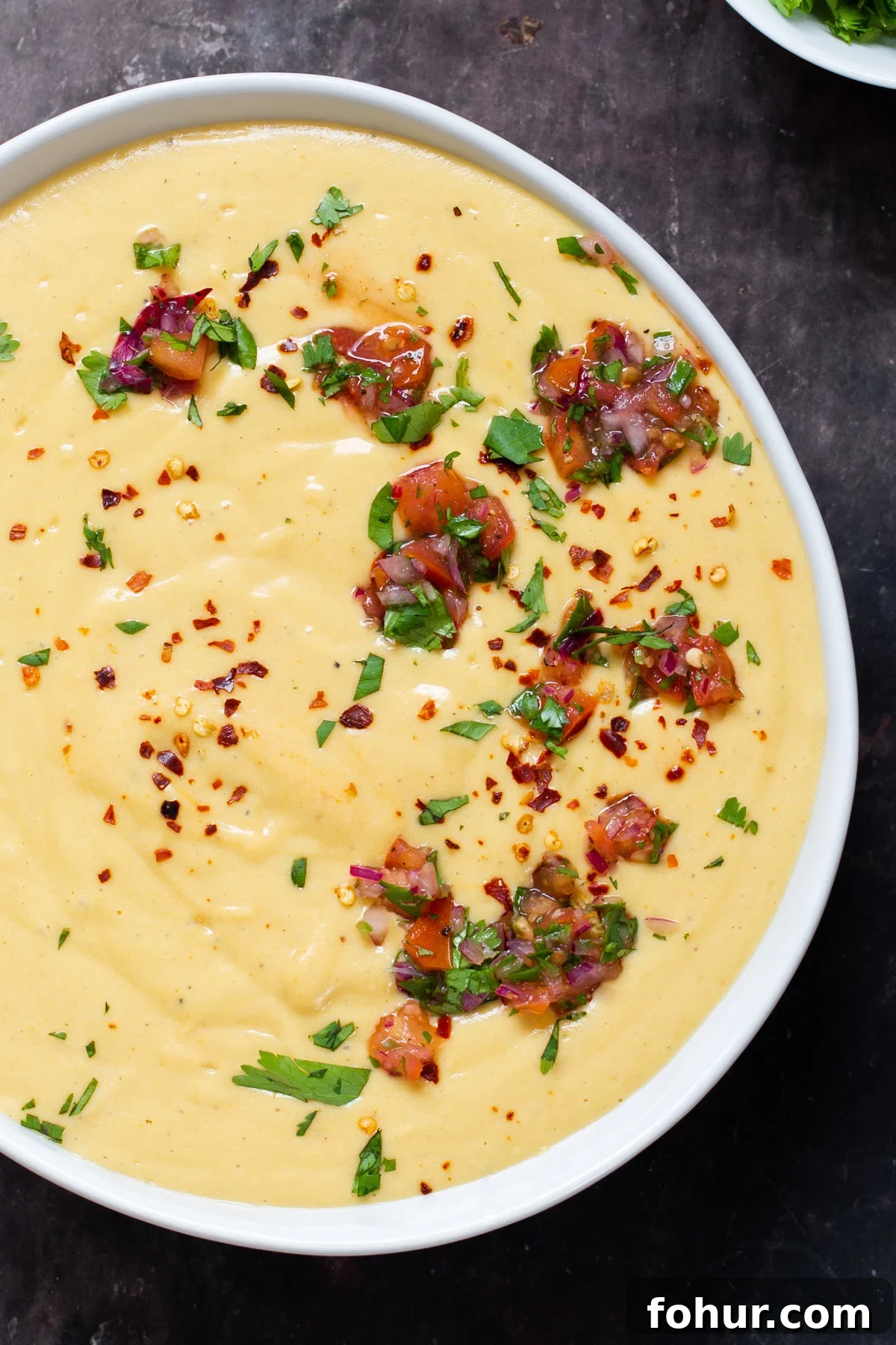 Instant Pot Vegan Cheese Sauce with Potatoes and Carrots 3 overhead shot of a bowl of vegan cheese sauce sprinkled with chopped herbs and tomatoes