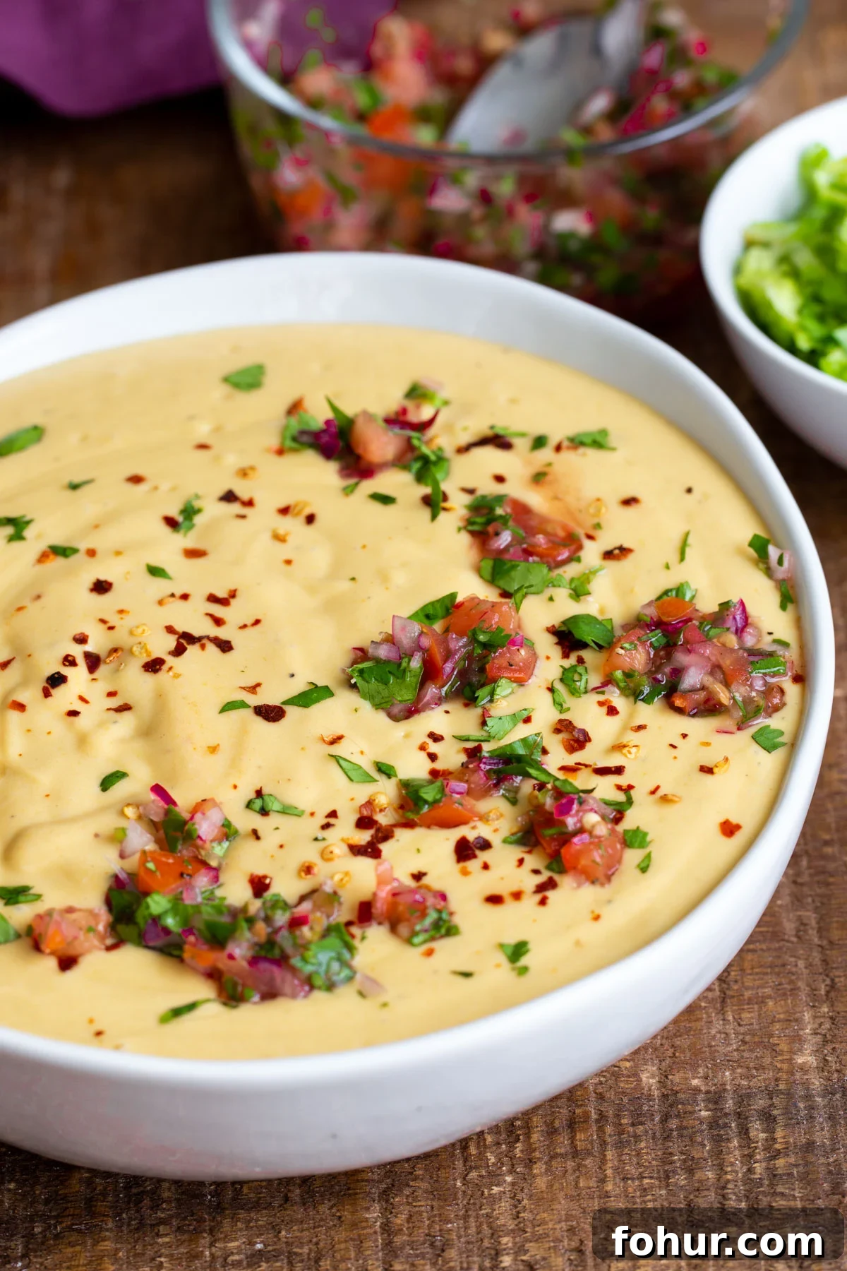 Instant Pot Vegan Cheese Sauce with Potatoes and Carrots 4 side view of a white bowl filled with vegan cheese sauce and sprinkled with herbs and chopped tomatoes
