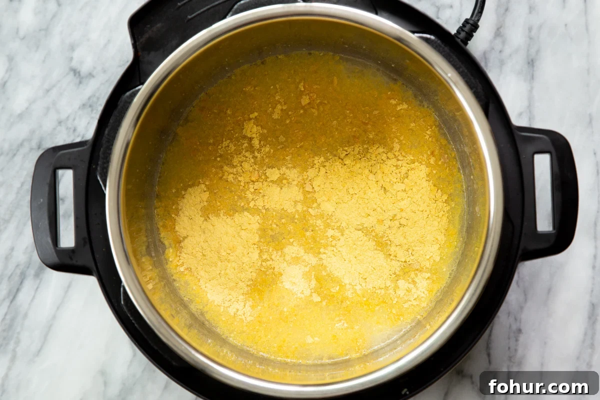 Instant Pot Vegan Cheese Sauce with Potatoes and Carrots 6 Nutritional yeast being added to an instant pot with ingredients for vegan cheese sauce