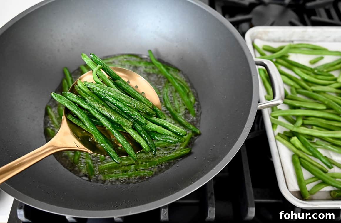 Stir-Fried Chinese Garlic Green Beans 3 Fried green beans in a slotted spoon held over a wok