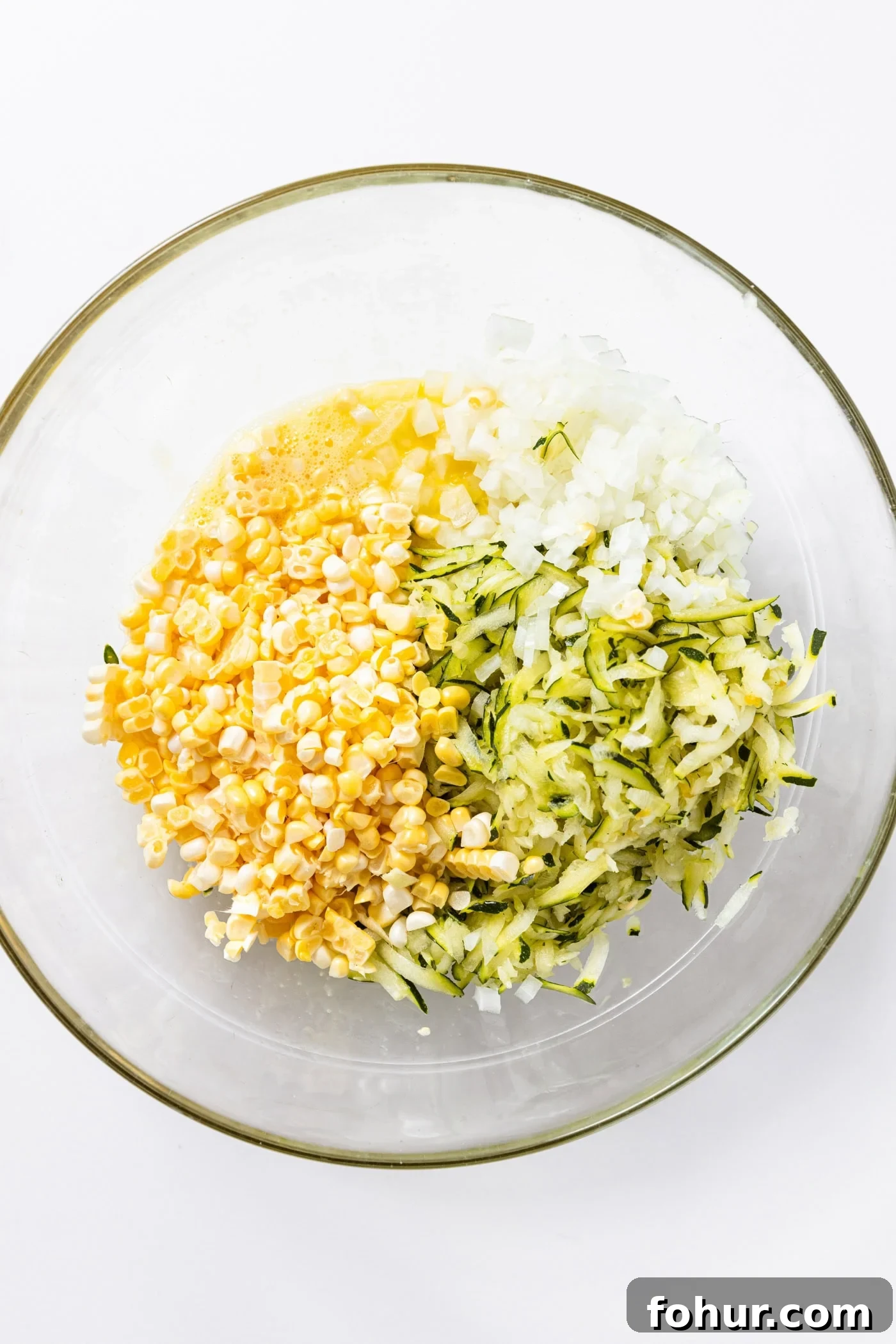Crispy Zucchini and Sweet Corn Fritters 5 Glass bowl sitting on white countertop filled with onion, corn, and zucchini.