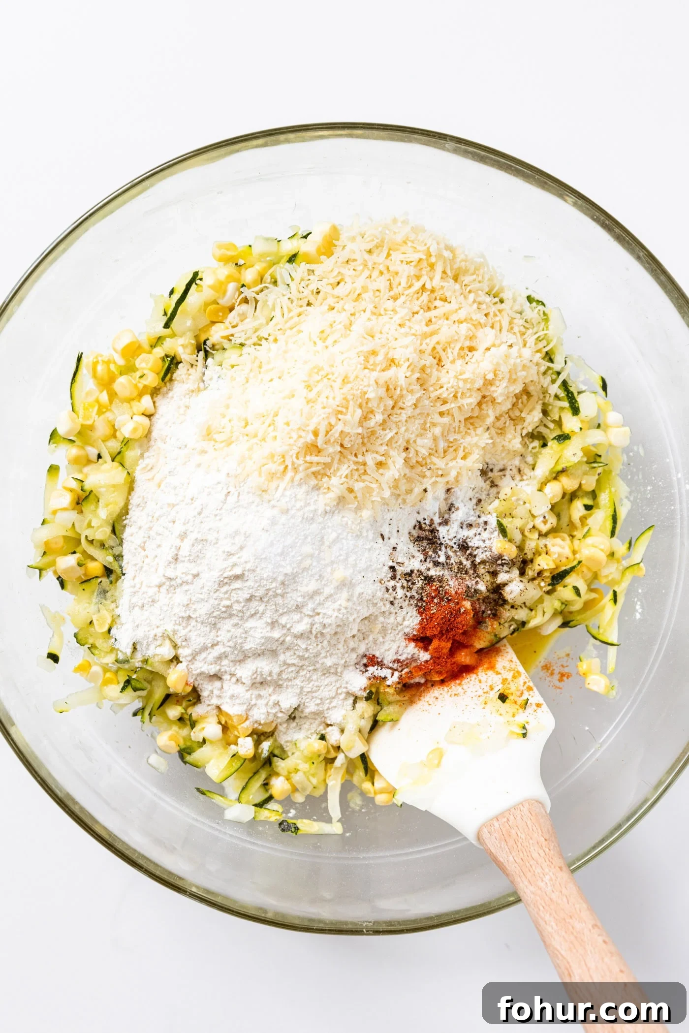 Crispy Zucchini and Sweet Corn Fritters 6 Corn and zucchini mixture sitting in glass bowl topped with flour, Parmesan cheese, and spices.