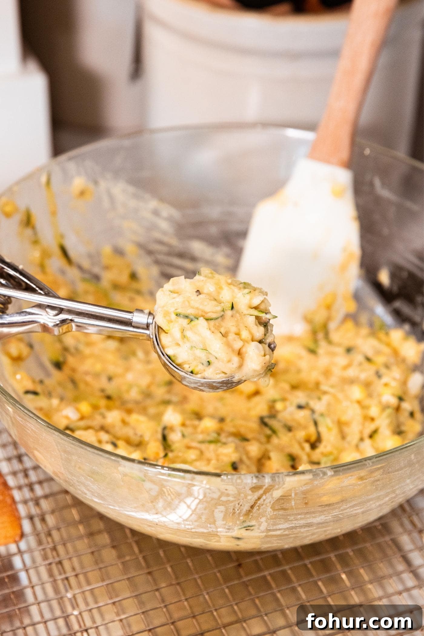 Crispy Zucchini and Sweet Corn Fritters 8 Hand holding small ice cream scoop with fritter batter inside.