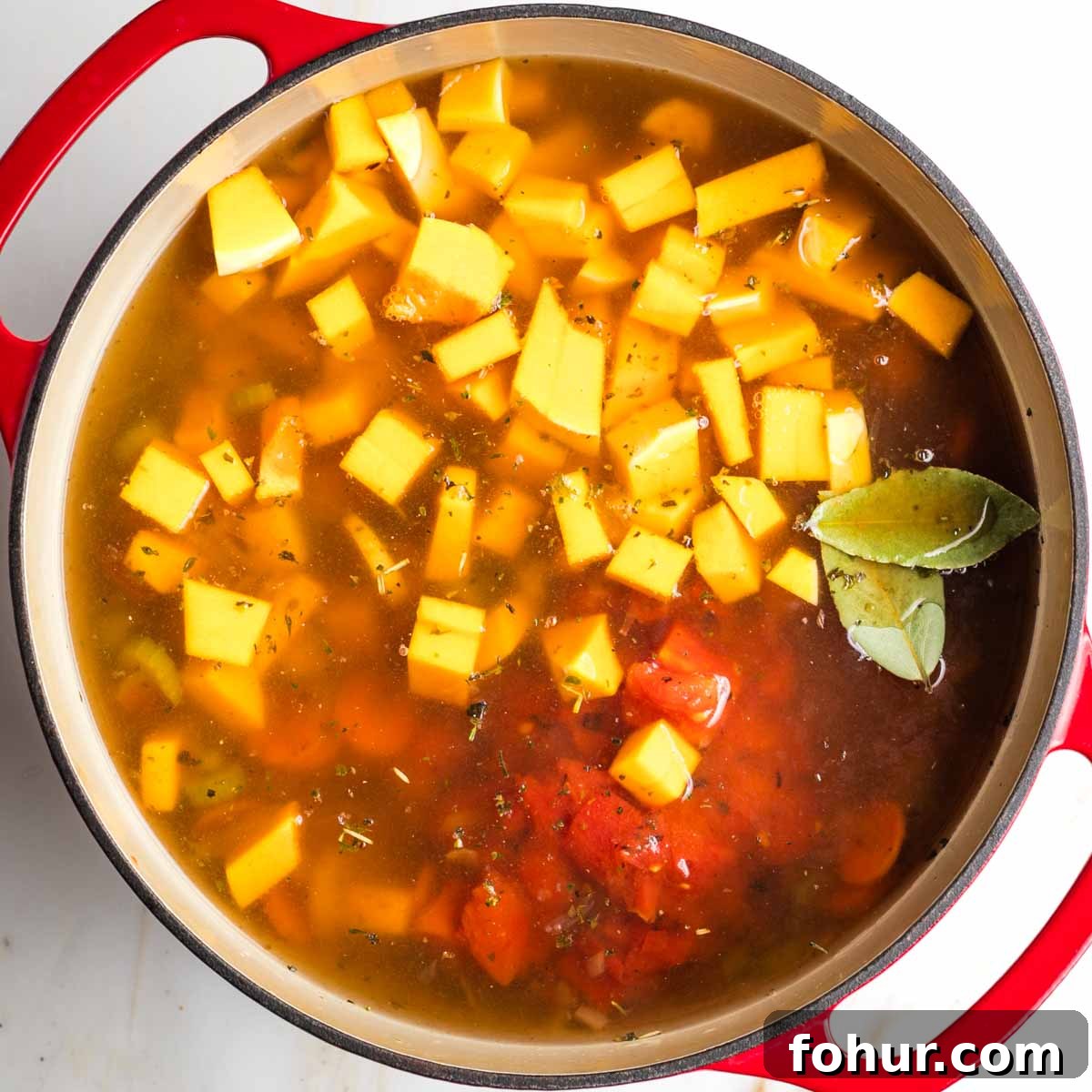 Vegan Fall Minestrone Soup with Roasted Autumn Vegetables 9 Cubes of butternut squash, diced tomatoes and bay leaves, floating in broth in a dutch oven.