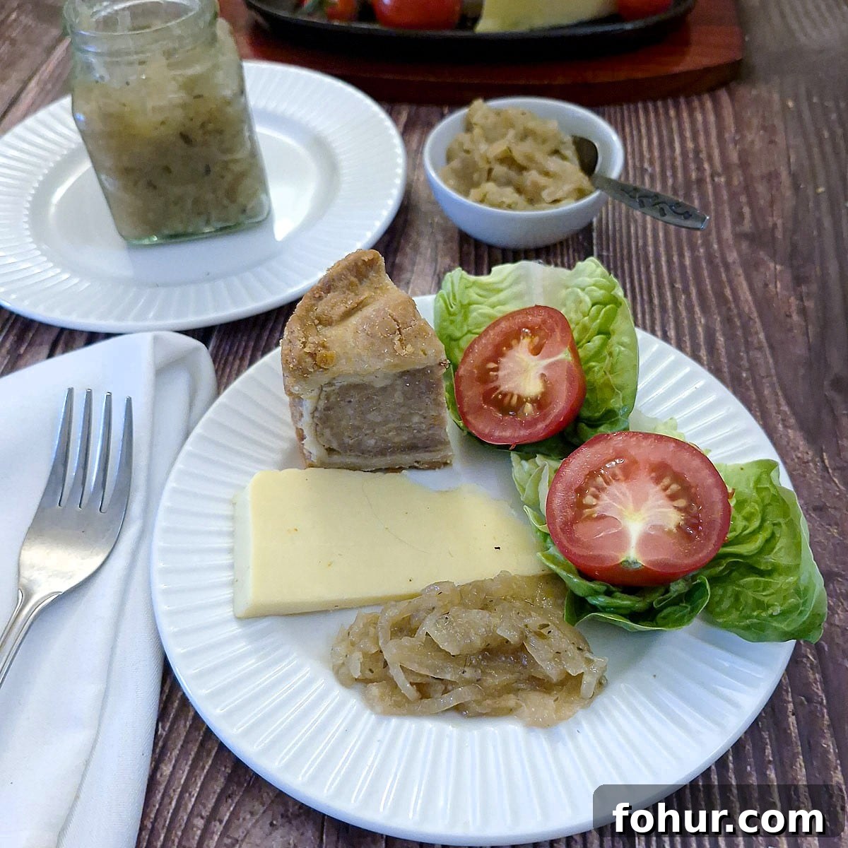 Caramelized Onion and Apple Marmalade Recipe 2 A small white plate piled with a pork pie, lettuce and tomato, cheese and a spoonful of onion marmalade.