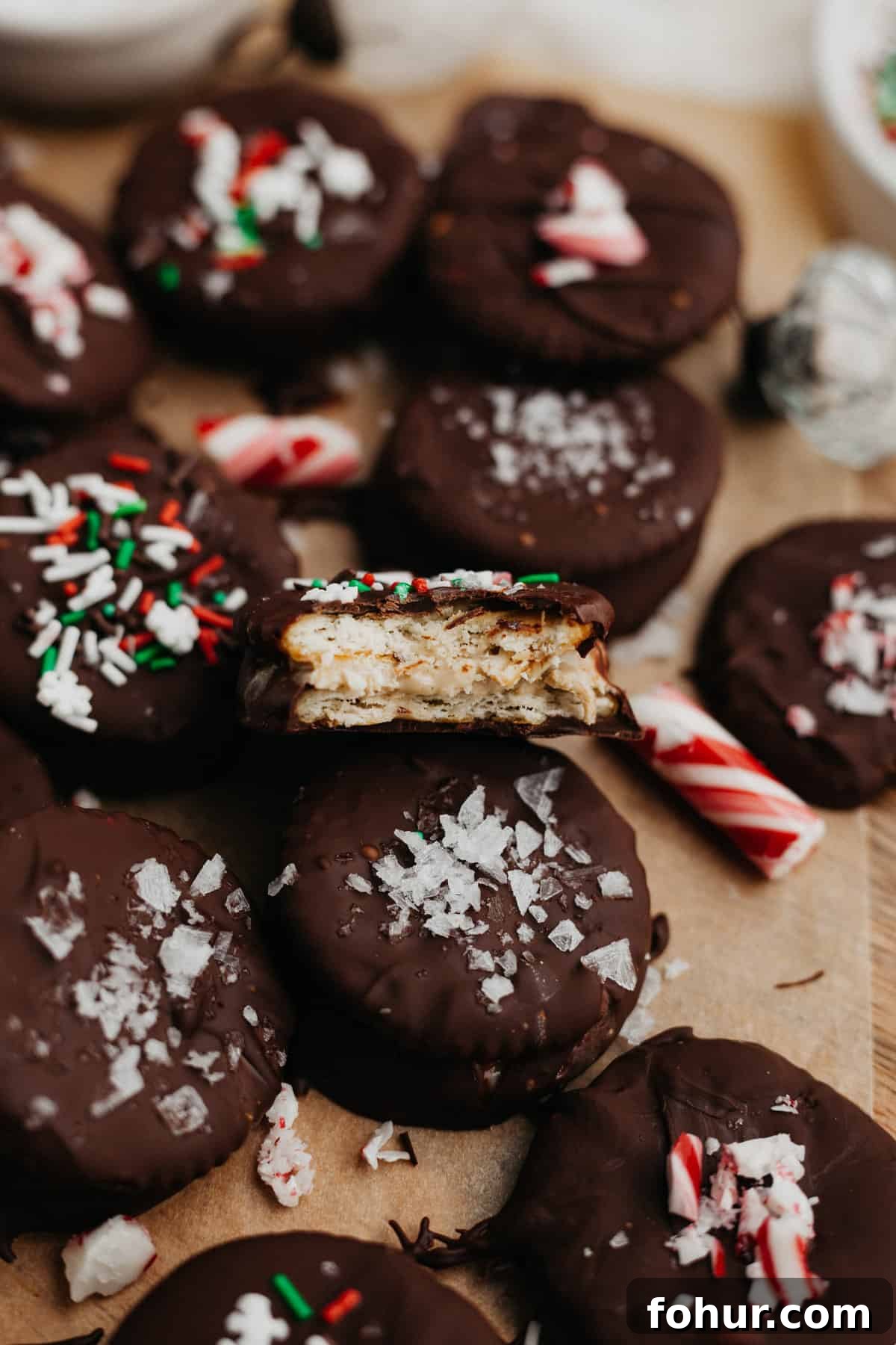 Chocolate no bake christmas cookies dipped in chocolate and topped with christmas sprinkles on parchment paper. One cookie has a bite taken out of it.