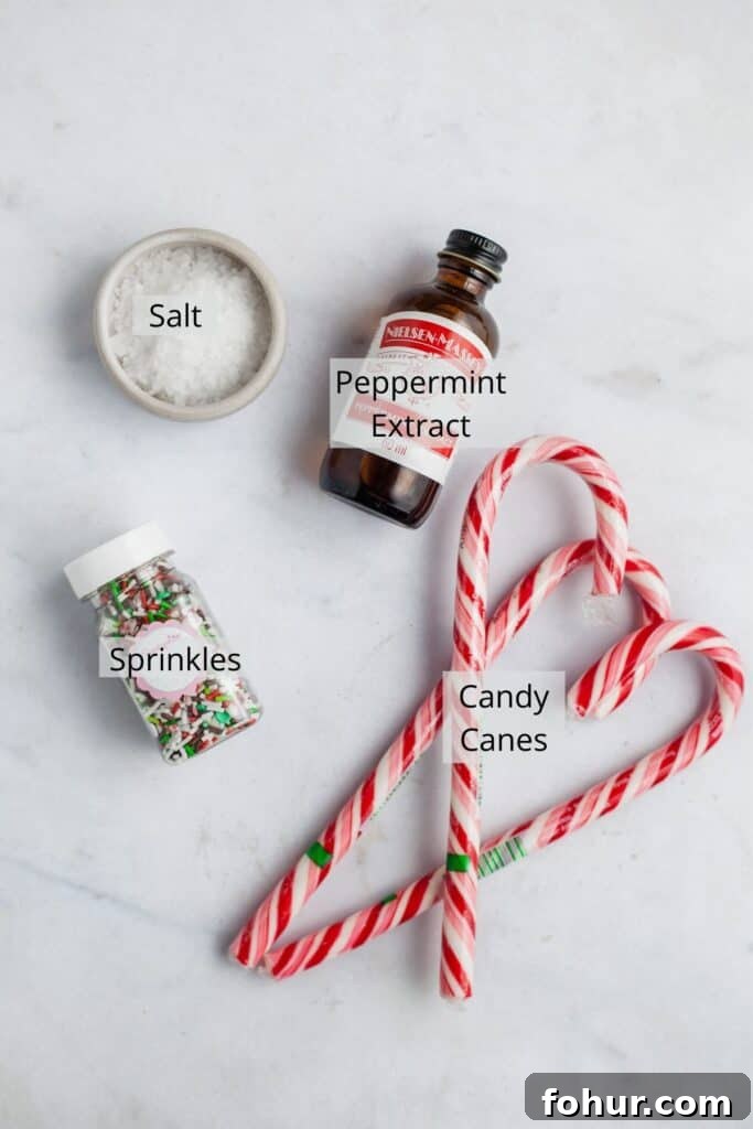 peppermint extract, three candy canes, sprinkles and a small bowl of salt on marble.