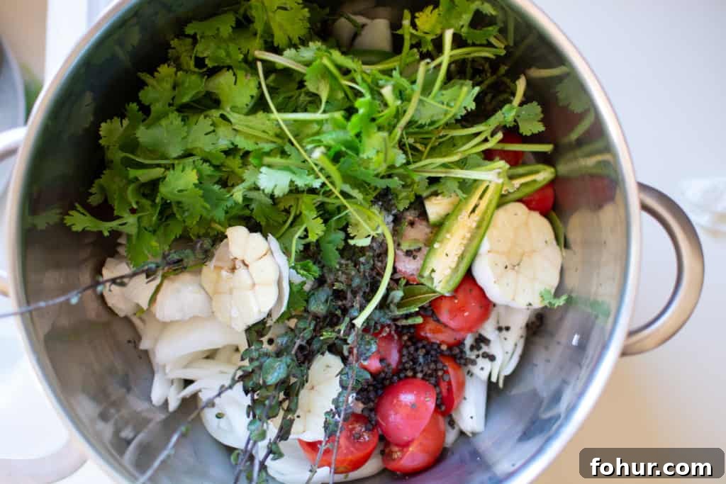 Large pot with poaching ingredients including cilantro, garlic, tomatoes and peppercorns