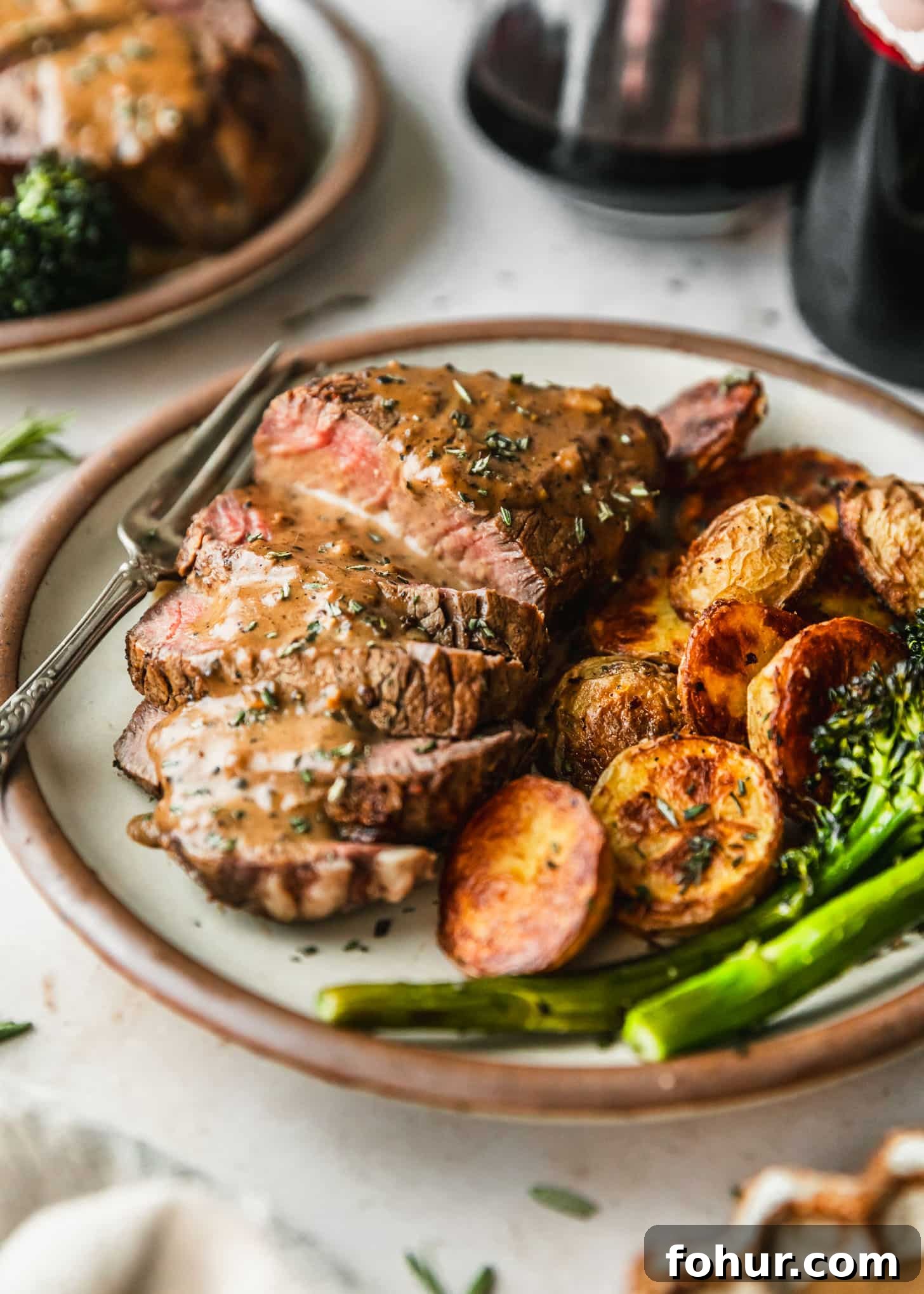 Reverse-Sear Filet Mignon Recipe with Creamy Peppercorn Sauce 6 Reverse sear filet mignon with peppercorn sauce, potatoes, and broccolini on a white plate next to red wine and a beige linen with a marble counter.