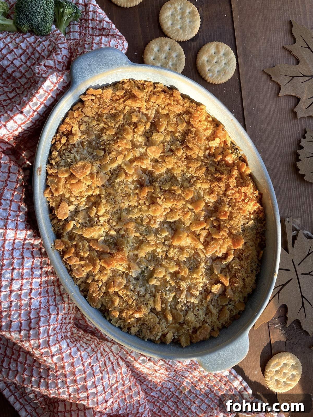Creamy Southern Broccoli Casserole Recipe 2 A blue casserole dish filled with baked broccoli casserole topped with ritz crackers and a red tea towel.
