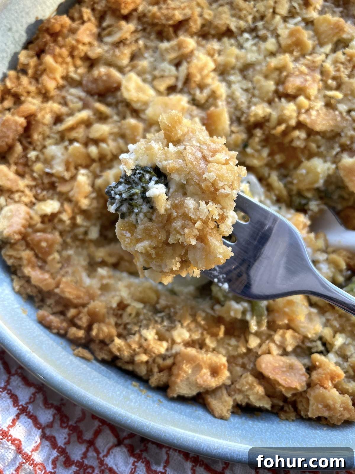 Creamy Southern Broccoli Casserole Recipe 7 A bite of broccoli casserole on a fork held over a dish of broccoli casserole.