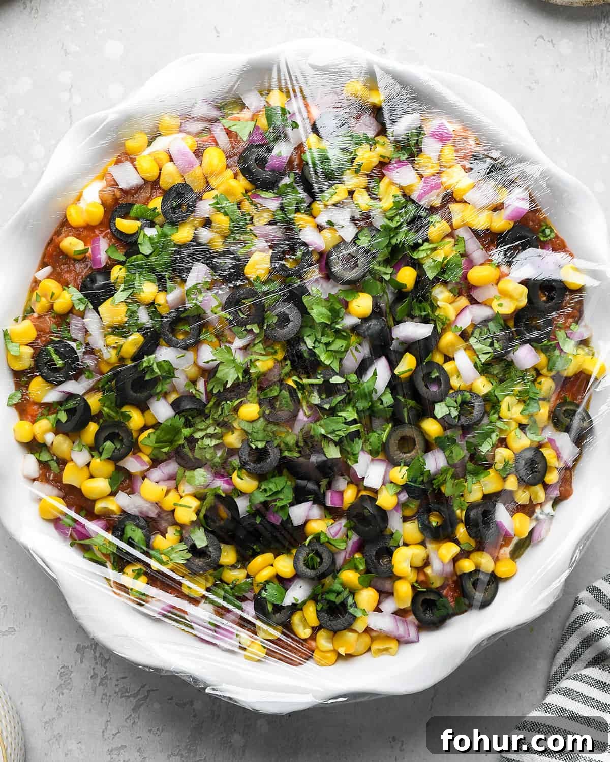 Authentic Mexican Seven Layer Dip Recipe 9 Mexican 7 Layer Dip in a pie dish covered in plastic wrap to chill