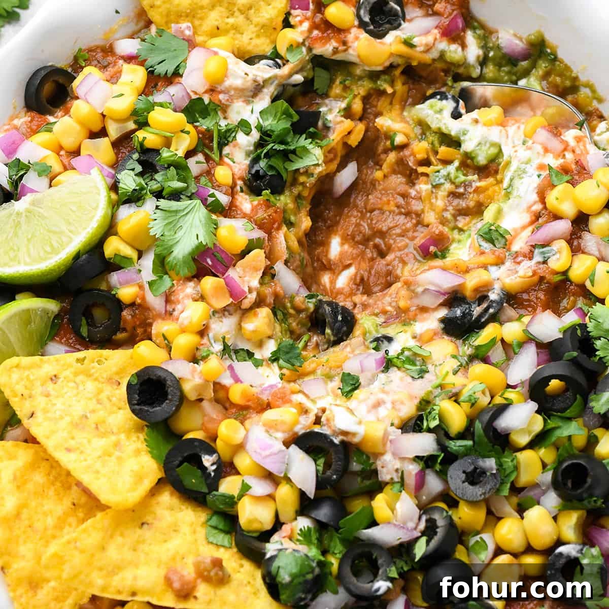 Authentic Mexican Seven Layer Dip Recipe 12 a spoon scooping Mexican 7 Layer Dip out of a pie dish