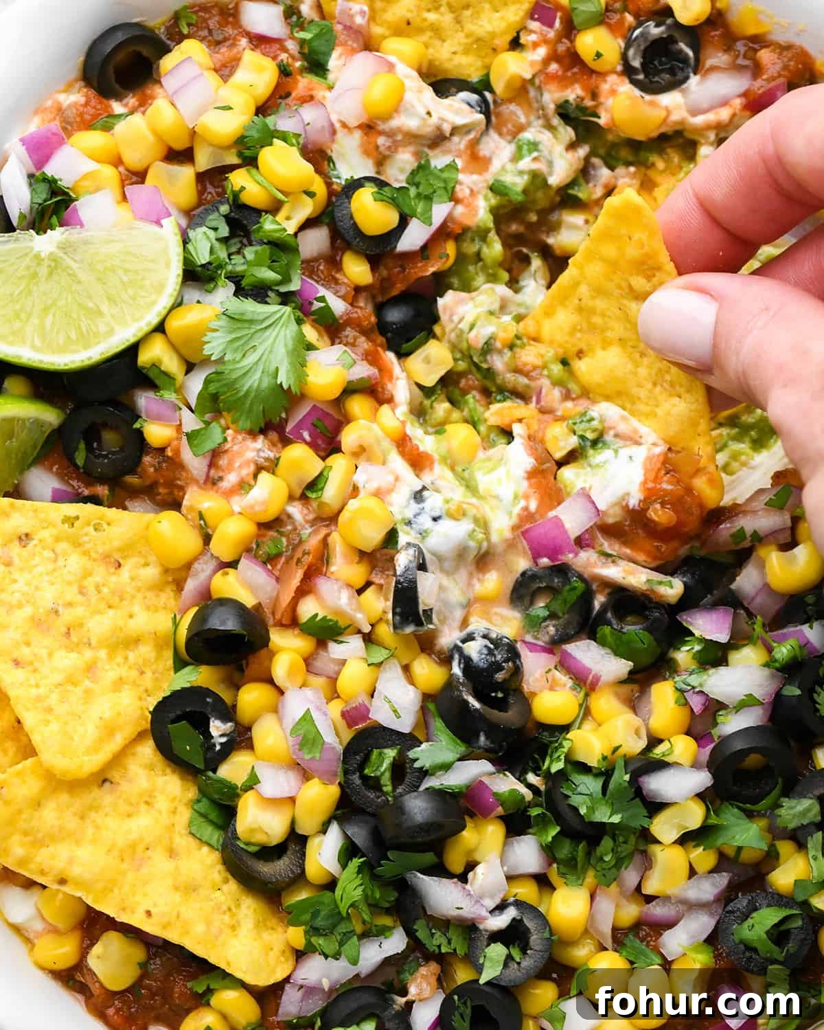 Authentic Mexican Seven Layer Dip Recipe 2 a chip dipping in a dish of Mexican 7 Layer Dip
