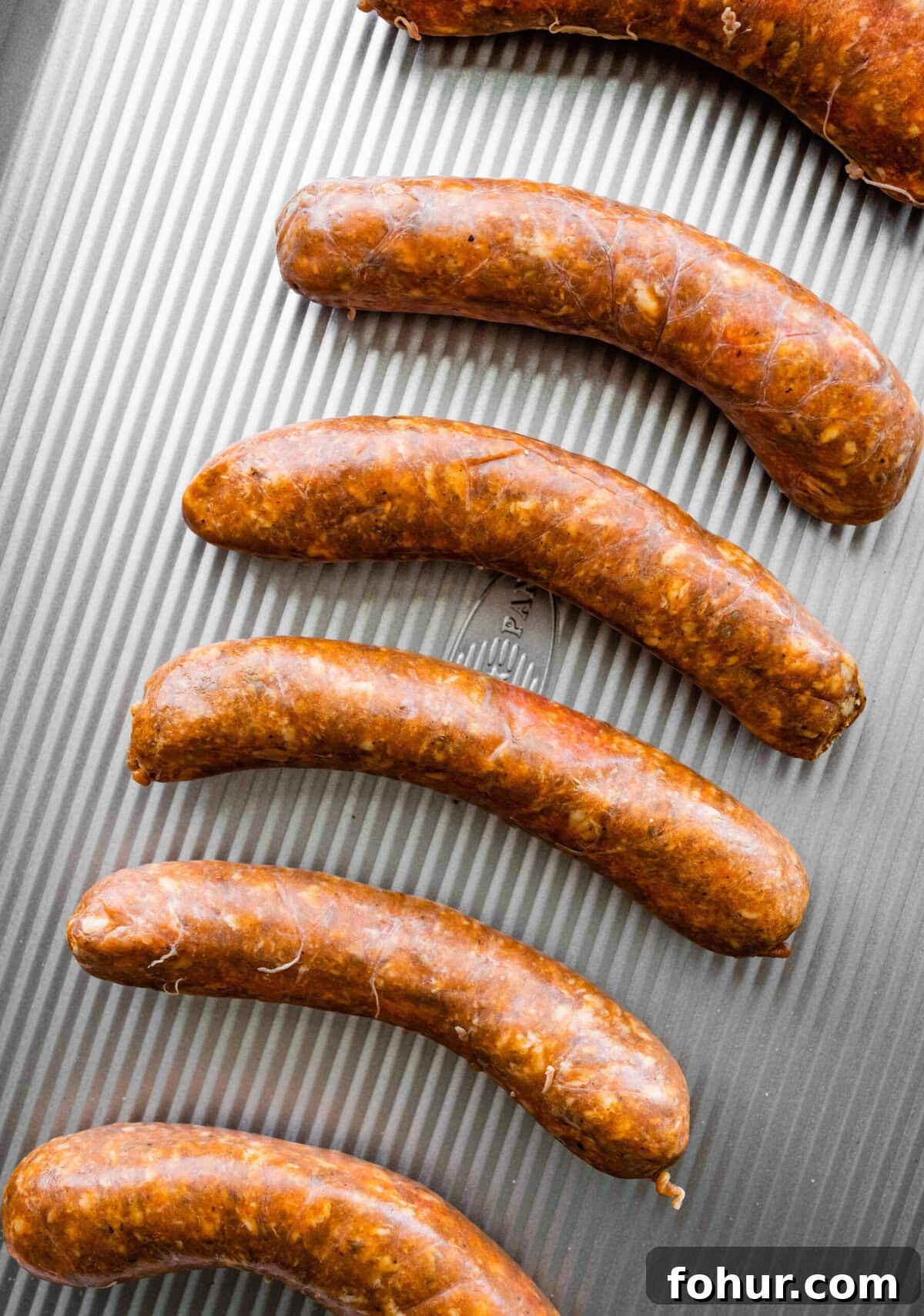 Oven Baked Italian Sausage Recipe with Peppers and Onions 4 uncooked Italian sausage on a baking sheet.