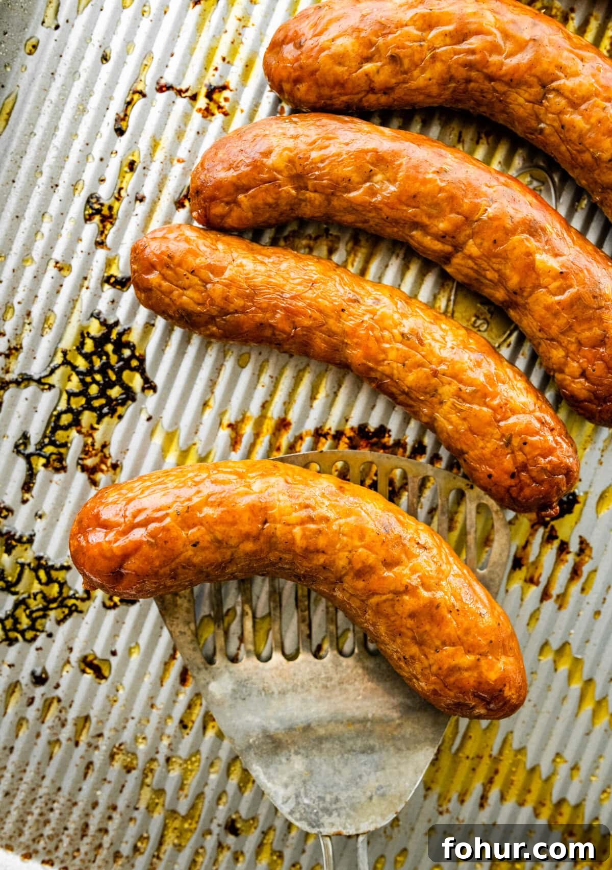 Oven Baked Italian Sausage Recipe with Peppers and Onions 5 Italian sausage on a baking sheet with a spatula lifting one.