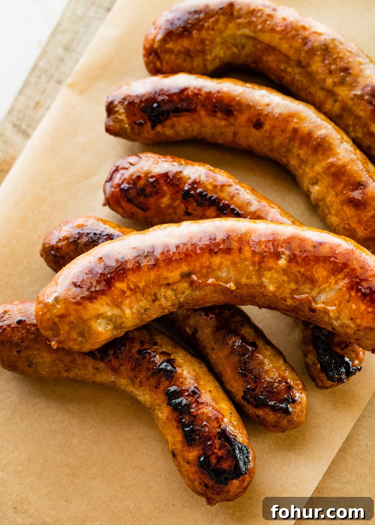 Oven Baked Italian Sausage Recipe with Peppers and Onions 6 Italian sausages on parchment paper and wood board.