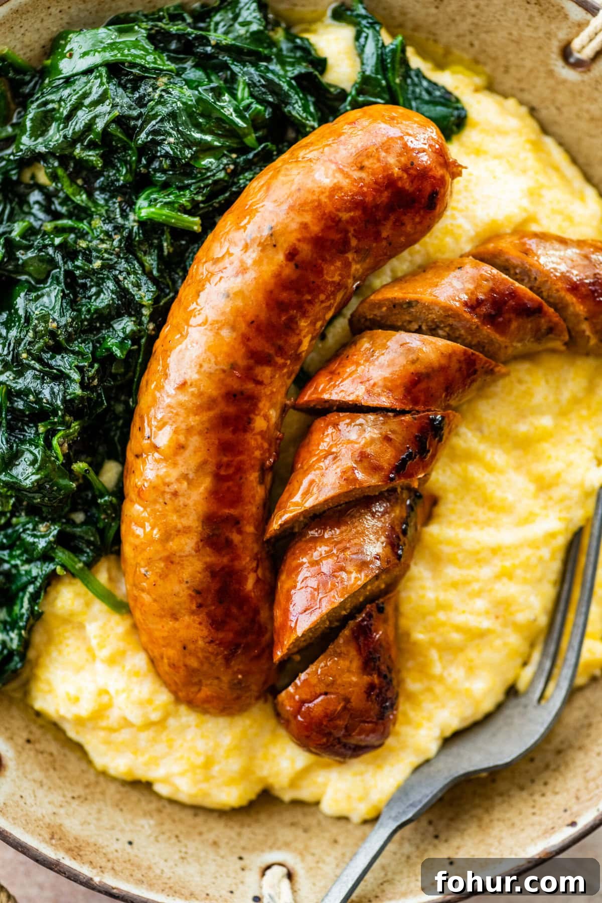 Oven Baked Italian Sausage Recipe with Peppers and Onions 7 Italian baked sausage in a bowl with polenta and cooked greens. Sausage is cut into slices.