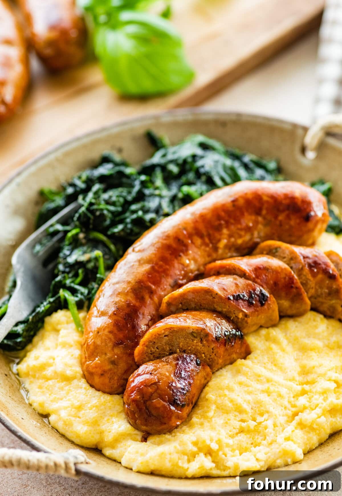 Oven Baked Italian Sausage Recipe with Peppers and Onions 8 Italian baked sausage in a bowl with polenta and cooked greens. Sausage is cut into slices.