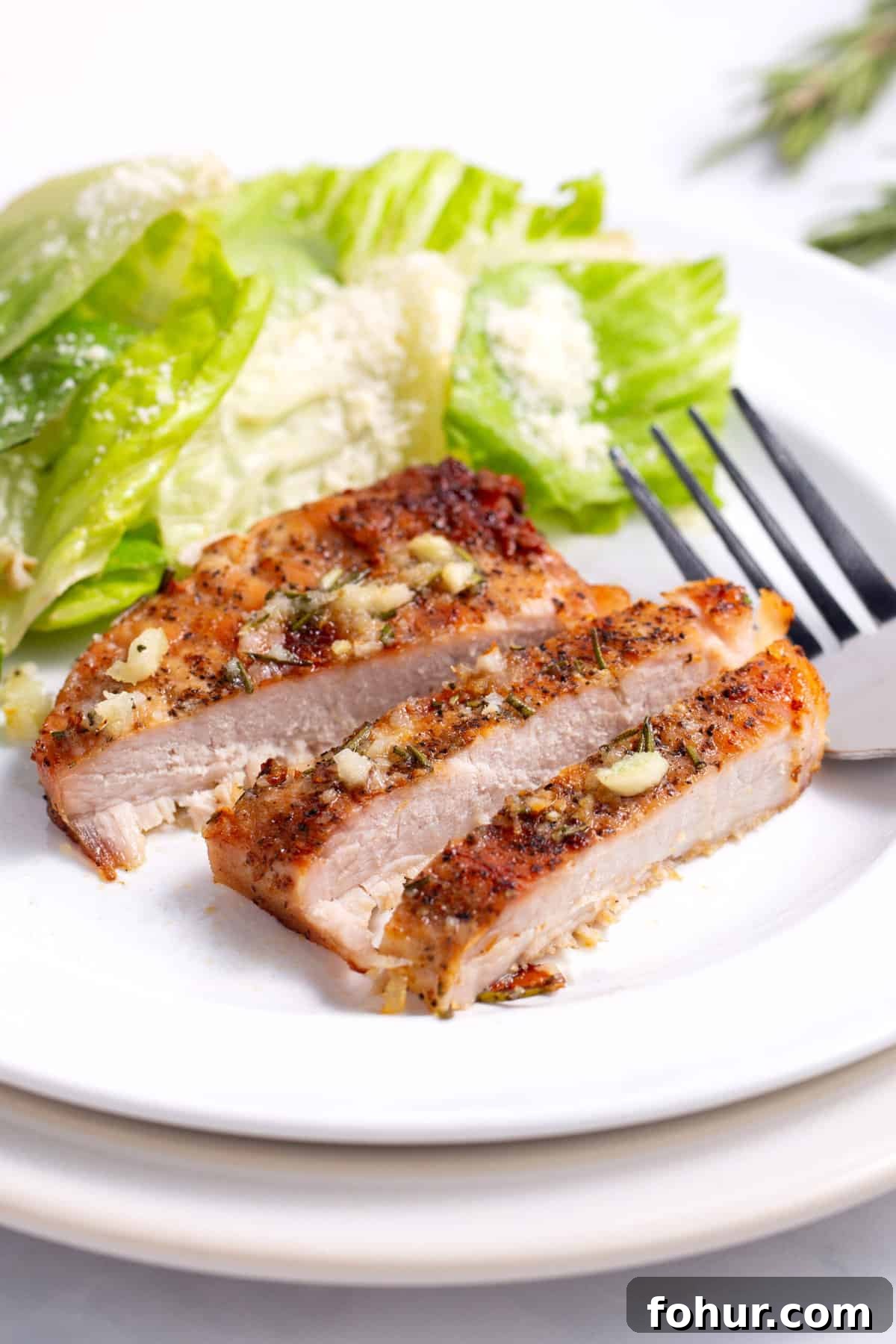baked pork chop sliced and served on a white round plate with a side salad