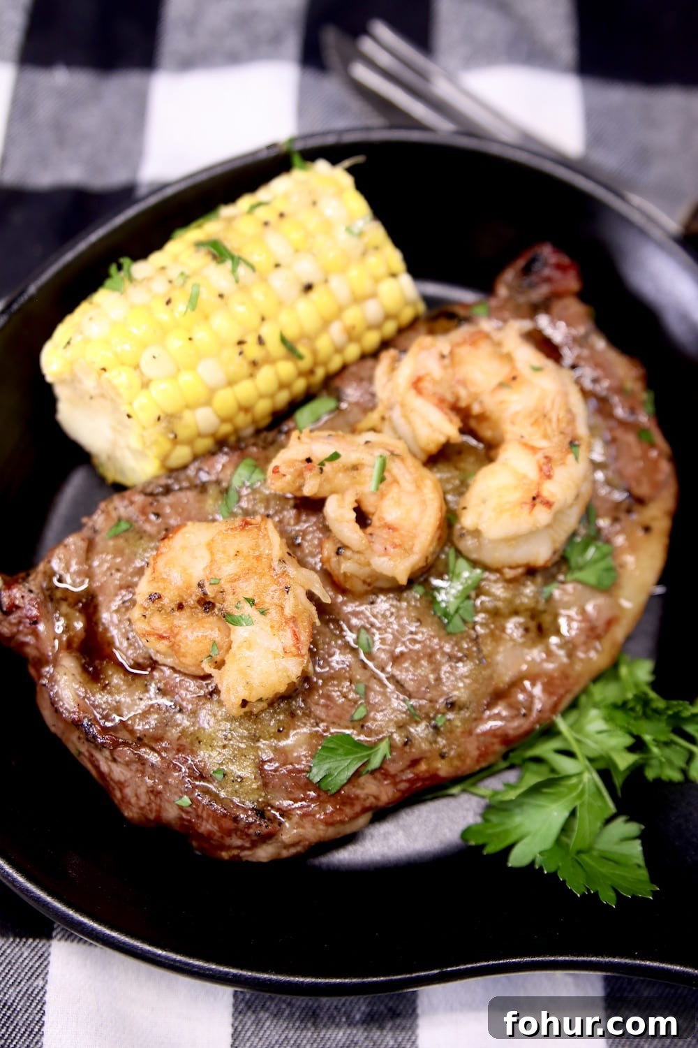 black serving skillet with ribeye steak topped with shrimp. Served with corn on the cob