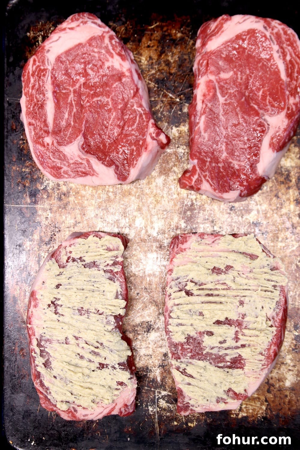 4 ribeye steaks on a sheet pan 2 topped with butter