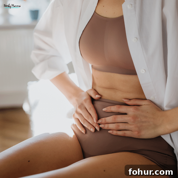 Postpartum Recovery: Roadmap to Long-Term Well-Being 2 A woman dressed in a brown bra and high-waisted underwear holds her stomach while sitting on a bed, showing postpartum healing.