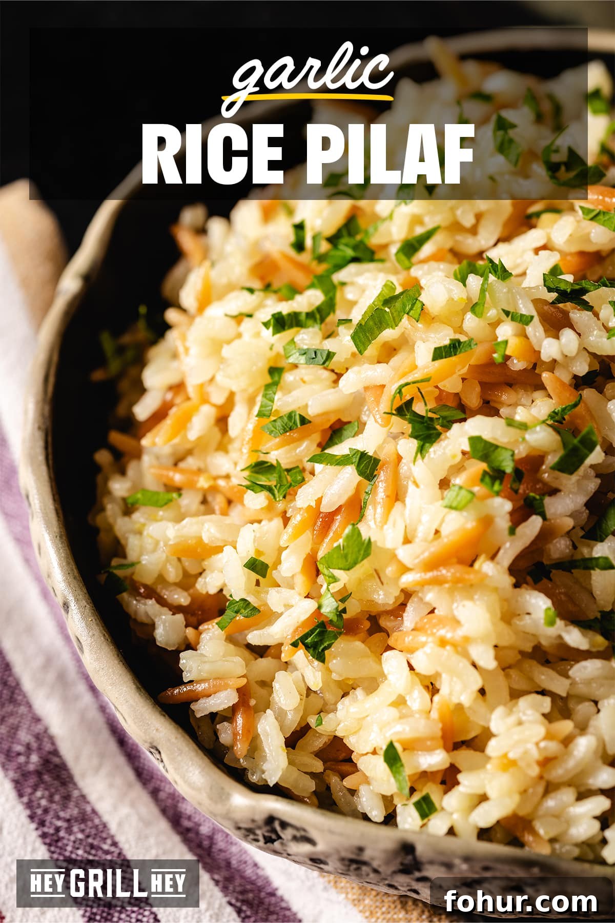 Savory Garlic Rice Pilaf with Lemon and Herbs 2 A zoomed in shot of a cream-colored bowl filled with a mixed rice garnished with fresh herbs. The text overlay reads 'Garlic Rice Pilaf' at the top, and 'Hey Grill Hey' at the bottom.