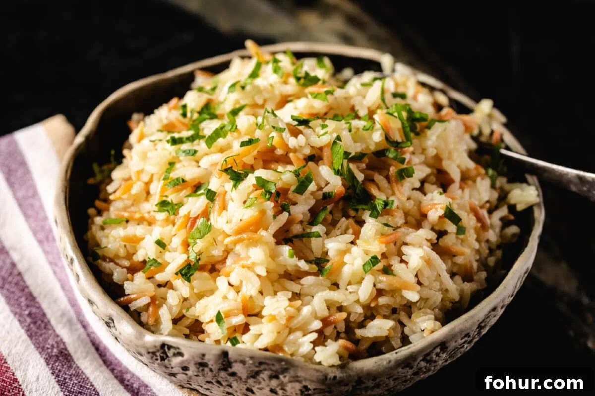 Savory Garlic Rice Pilaf with Lemon and Herbs 6 A cream-colored bowl sitting on a striped tablecloth. The bowl is filled with a rice dish garnished with fresh herbs, and has a spoon resting in it.
