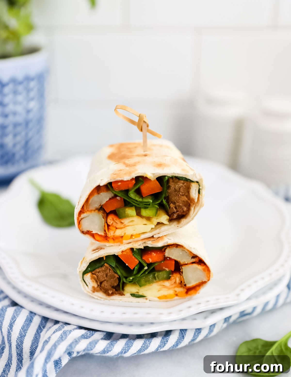 Vegan Breakfast Burrito Recipe with Tofu, Beans and Avocado 5 A burrito that has been sliced in half and stacked on top of itself. Inside is vegan egg, vegan sausage, peppers, spinach, breakfast potatoes