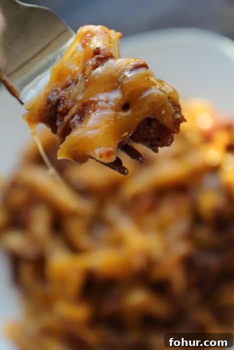 Slow Cooker Cheesy Beef Pasta Casserole Recipe (Video) 3 Fork with cheesy pasta beef casserole over a large bowl