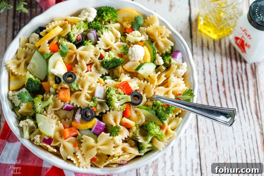Summer vegetables and farfalle pasta tossed with an Italian dressing in a white bowl.
