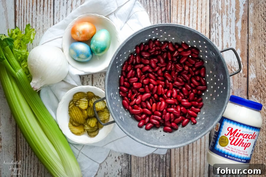 A colander full of drained kidney beans next to celery, onion, pickles, and hard boiled eggs.