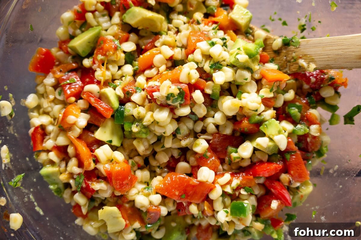 a bowl of mixed corn avocado salad with red peppers and herbs