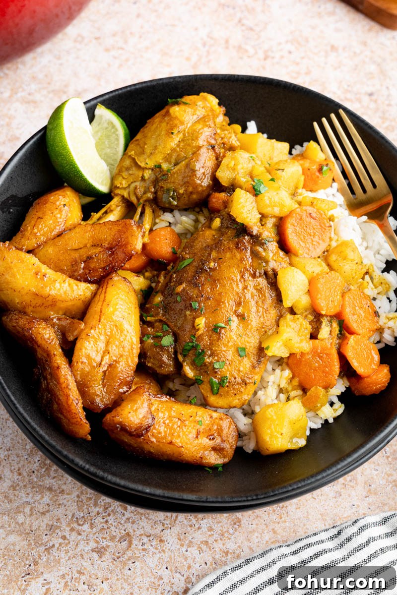 Authentic Jamaican Curry Chicken Recipe 5 Jamaican Curry Chicken on a plate with a side of white rice, sweet plantains and two lime wedges for serving.