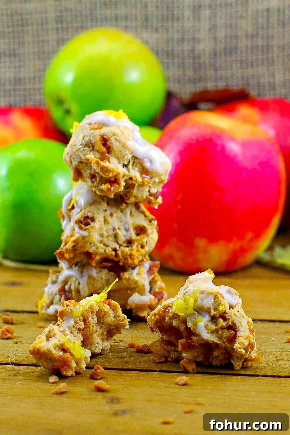 3 toffee apple cookies stacked and a split cookie in front with apples in the background.