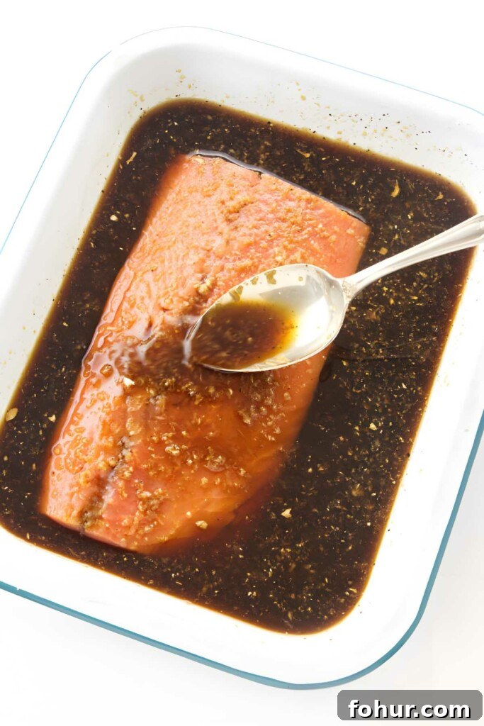 Bourbon Glazed Salmon Fillet Recipe 3 Raw salmon fillet in white dish, spooning dark marinade over fish.