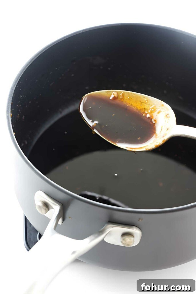 Bourbon Glazed Salmon Fillet Recipe 4 Metal spoon with dark sauce above black saucepan containing more sauce.