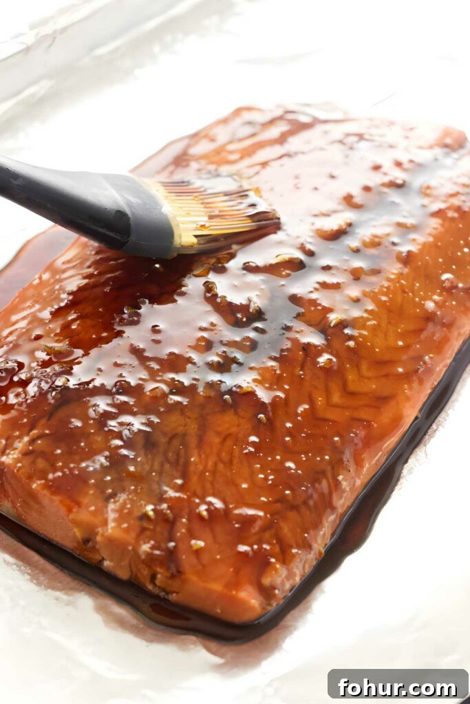 Bourbon Glazed Salmon Fillet Recipe 5 Brush applying glossy brown glaze to raw salmon fillet on foil.