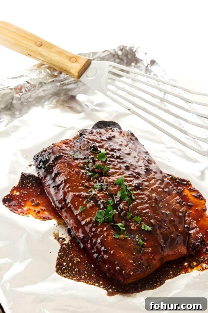 Bourbon Glazed Salmon Fillet Recipe 6 Glazed salmon on foil, garnished with herbs, beside a spatula.