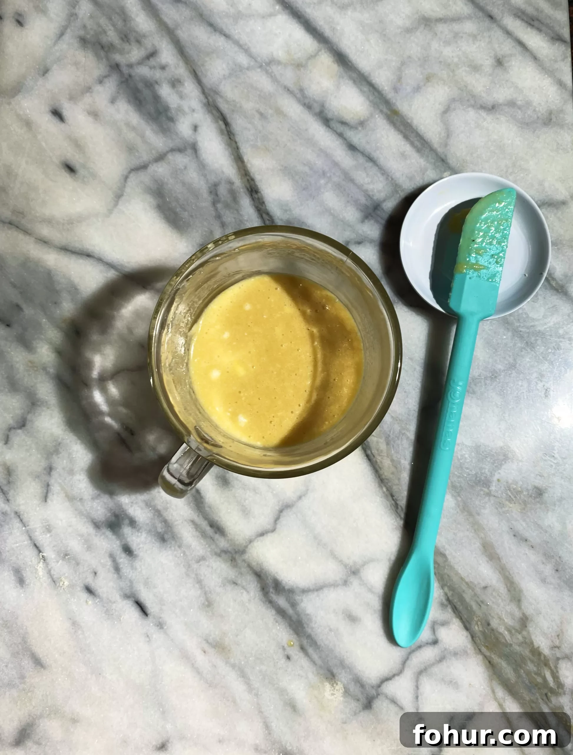 Almond Flour Mug Cake: Low-Carb Keto Microwave Dessert 4 Overhead shot of the batter combined together in a glass mug. spatula to the right.