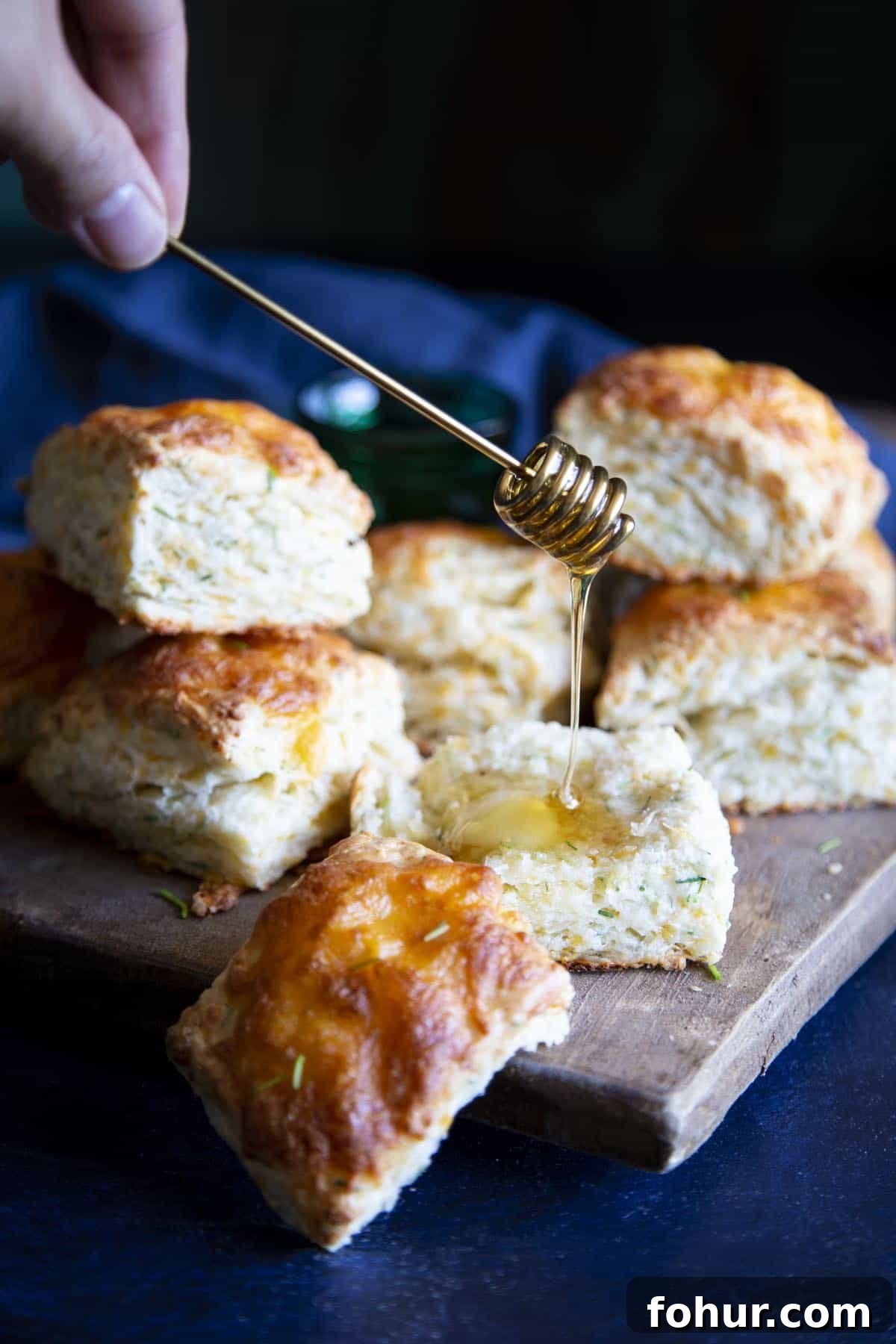 Flaky and Fluffy Cheese Biscuits with Chives Honey is being drizzled on a biscuit.