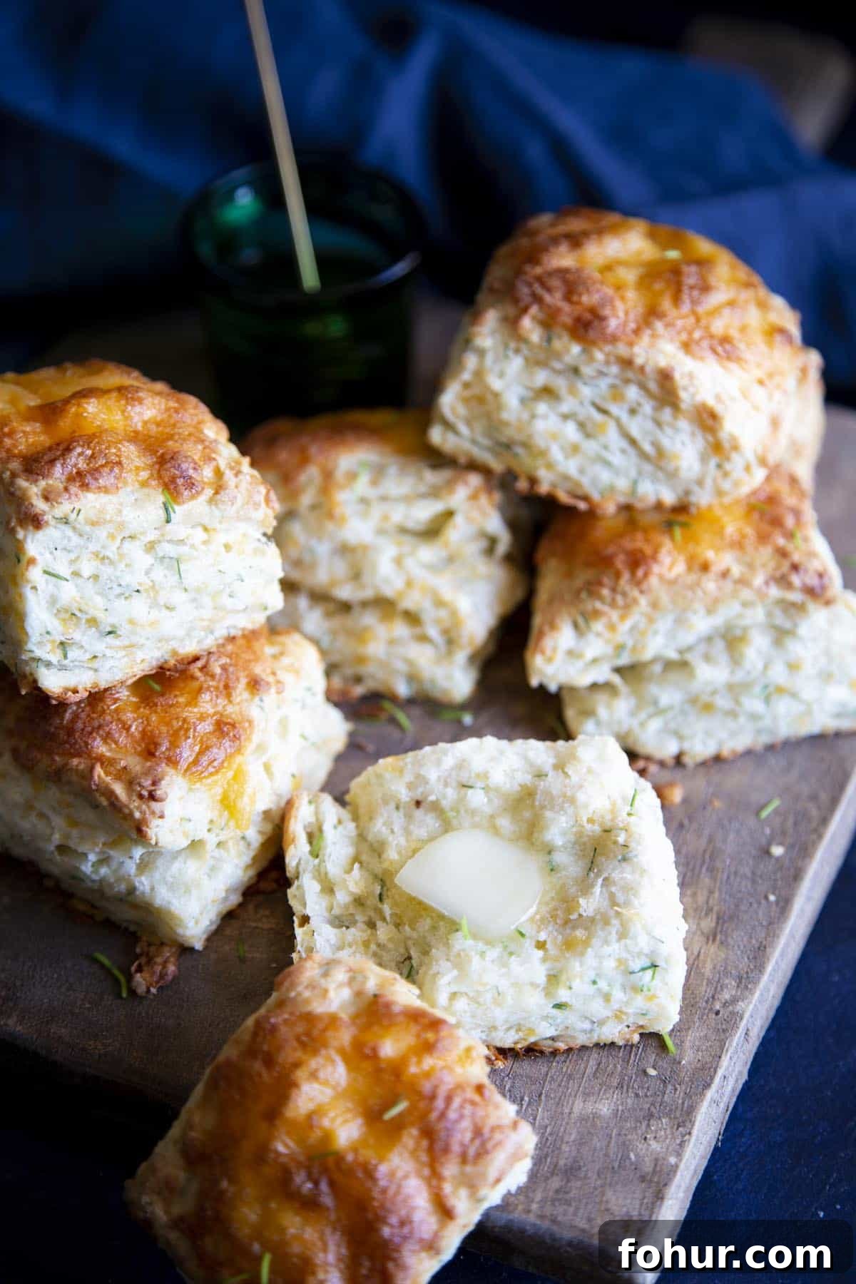 Flaky and Fluffy Cheese Biscuits with Chives Cheese biscuits on a wooden board, one is broken open with a pat of butter on it.